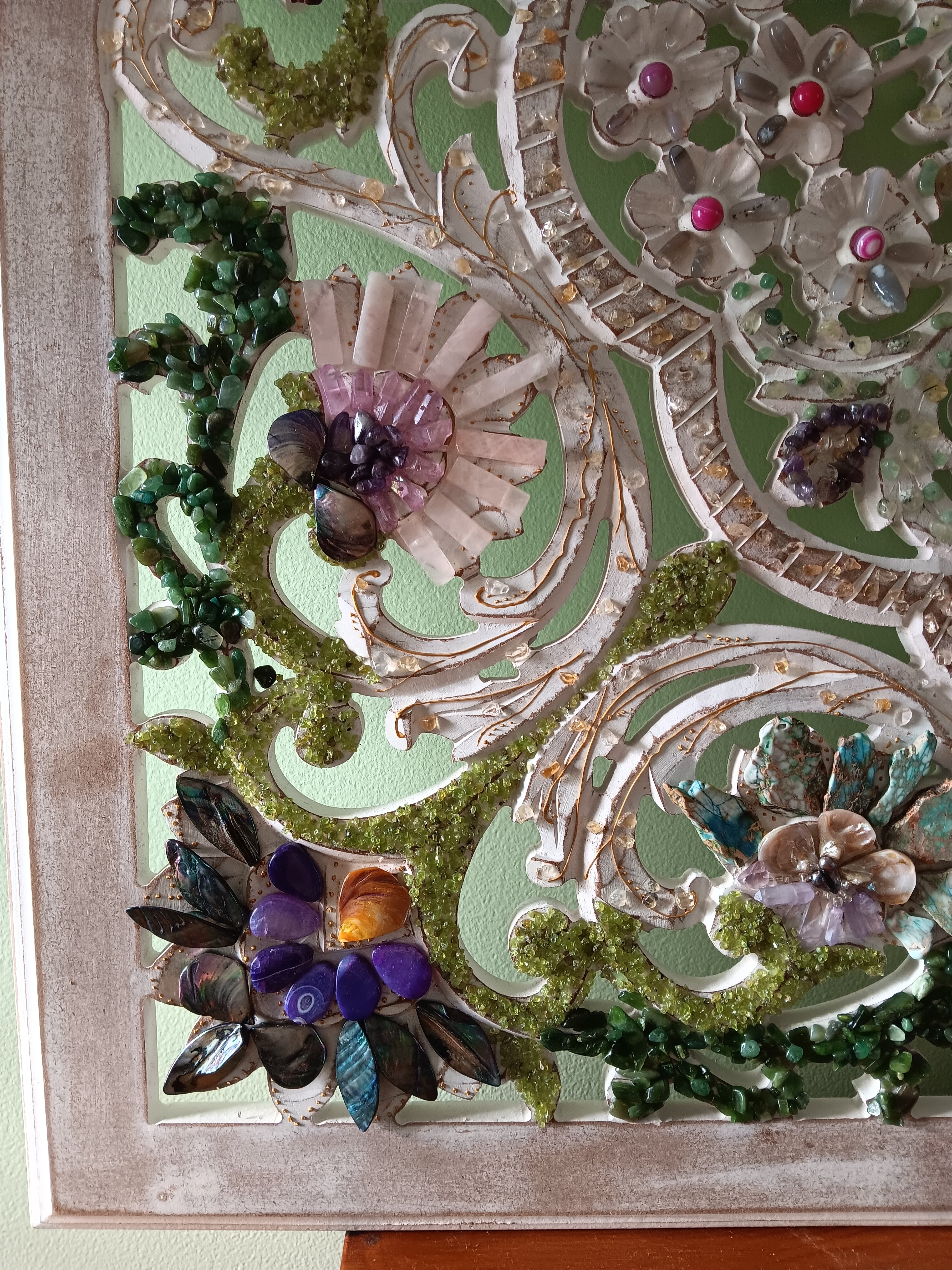 Decorative wall art with a floral design with semiprecious stones on wooden surface. 
