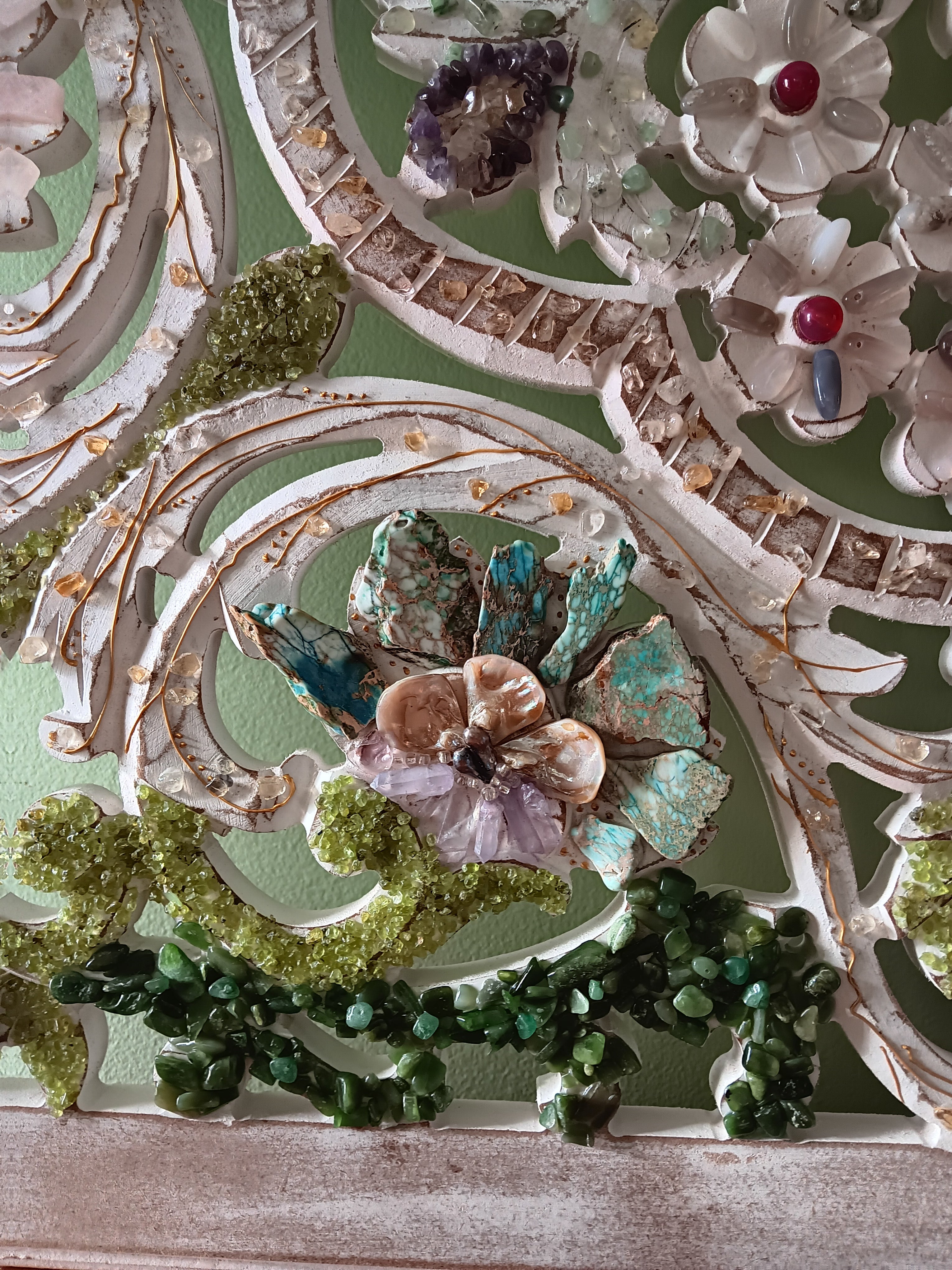 Decorative wall art with a floral design with semiprecious stones on wooden surface. 