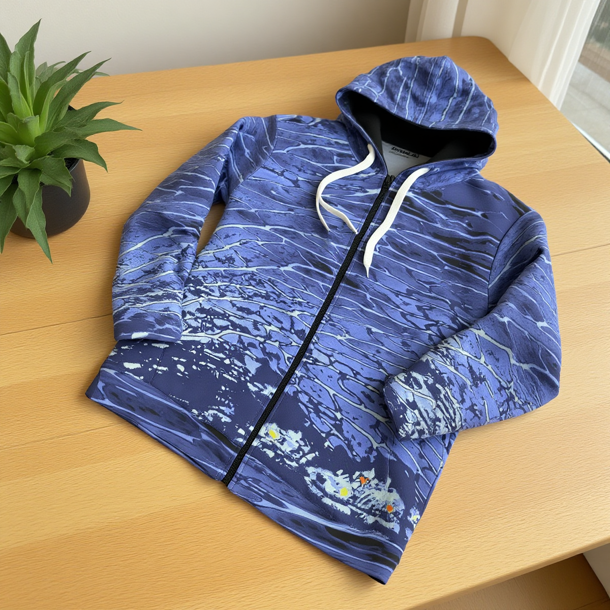Blue patterned hoodie on a wooden table with a plant in the background