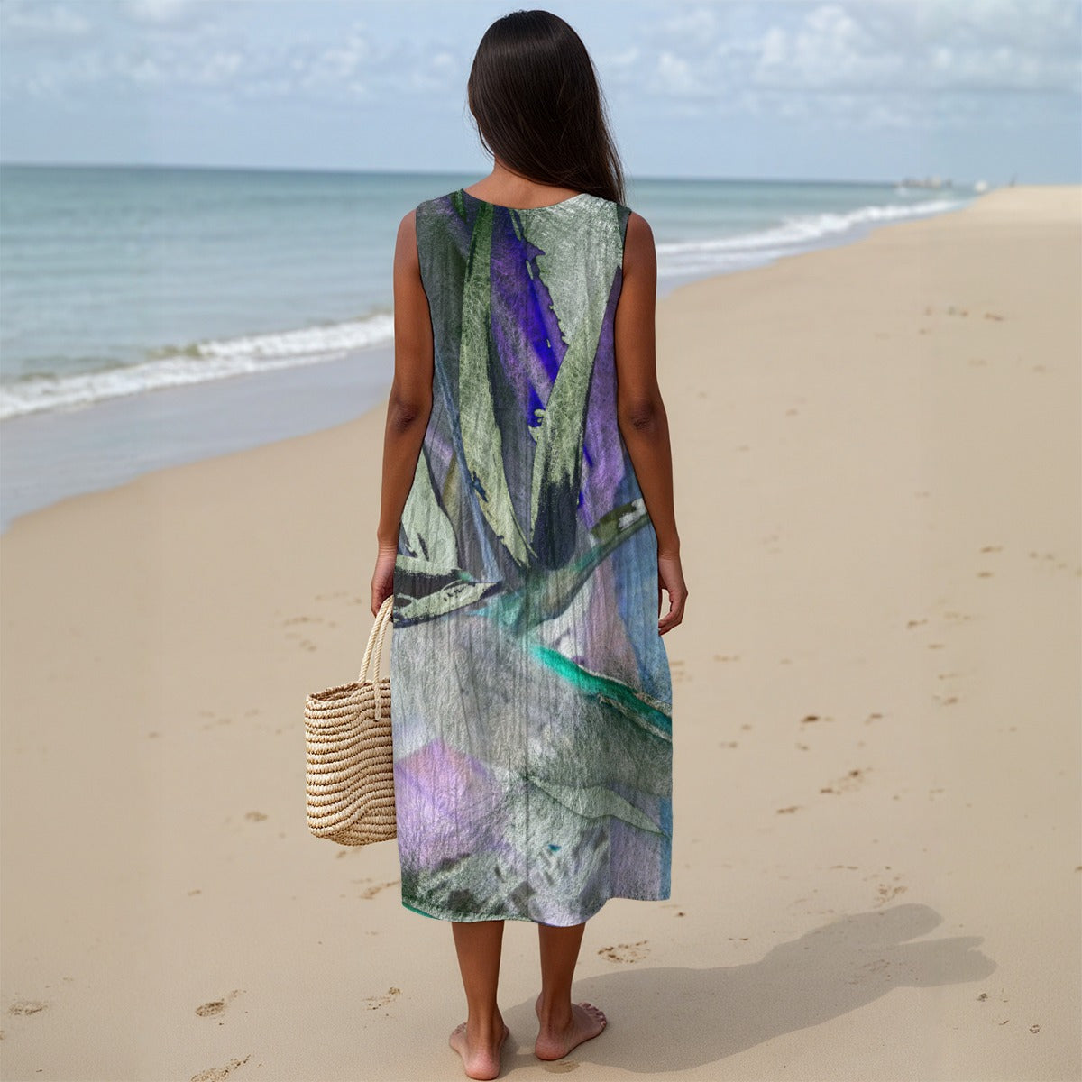 Person wearing a sleeveless, multicolored dress on a beach holding a woven bag.