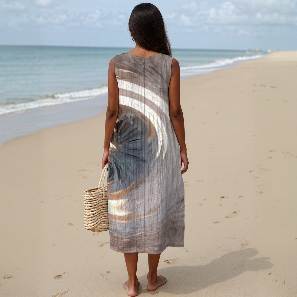 Woman in a long, light-colored dress standing on a sandy beach with ocean in the background.