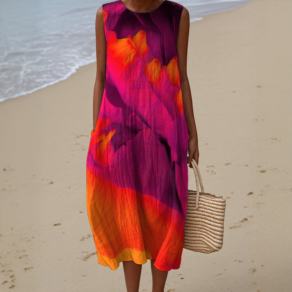 Person wearing a colorful dress on a beach holding a woven bag.