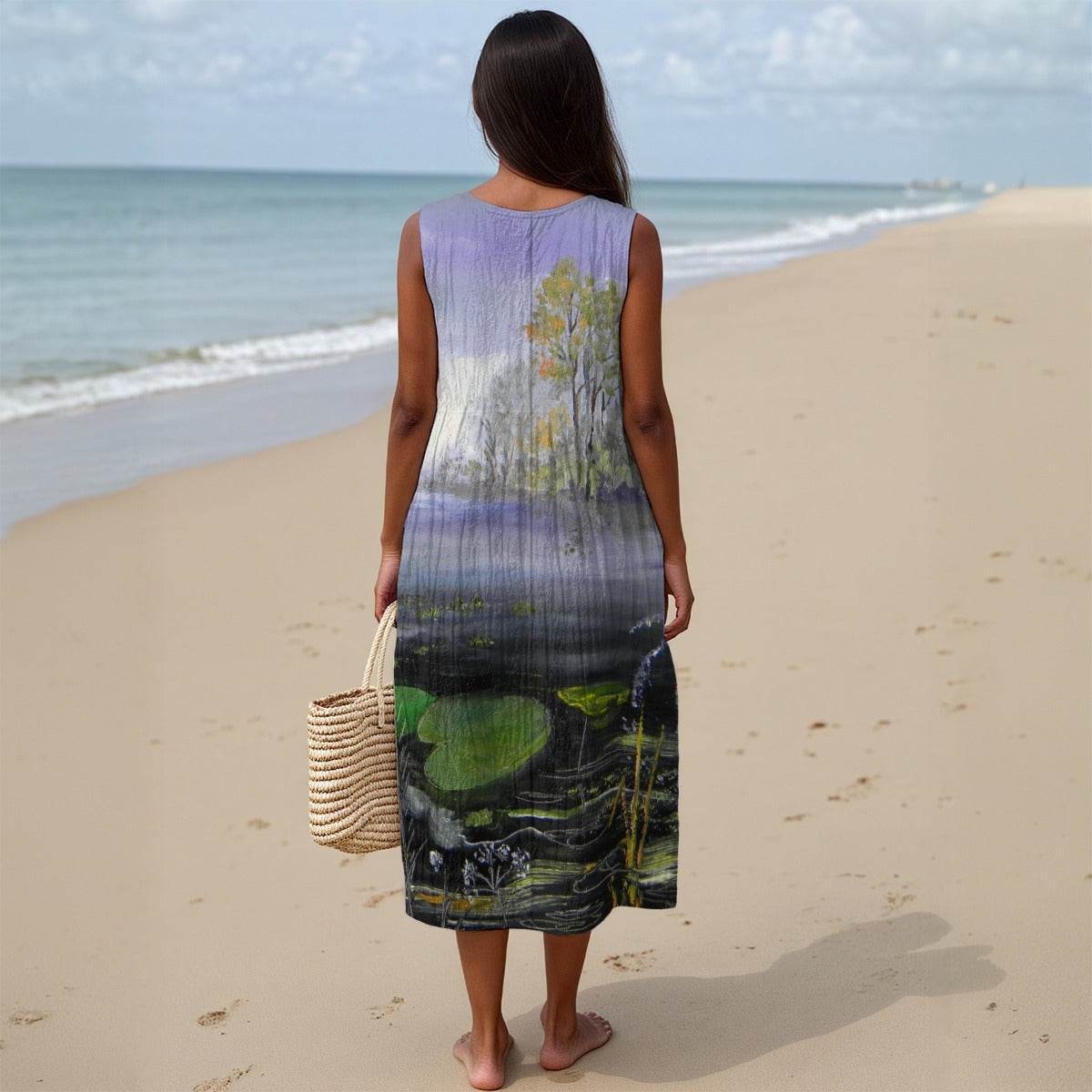 Woman in a sleeveless dress with nature print standing on a beach.