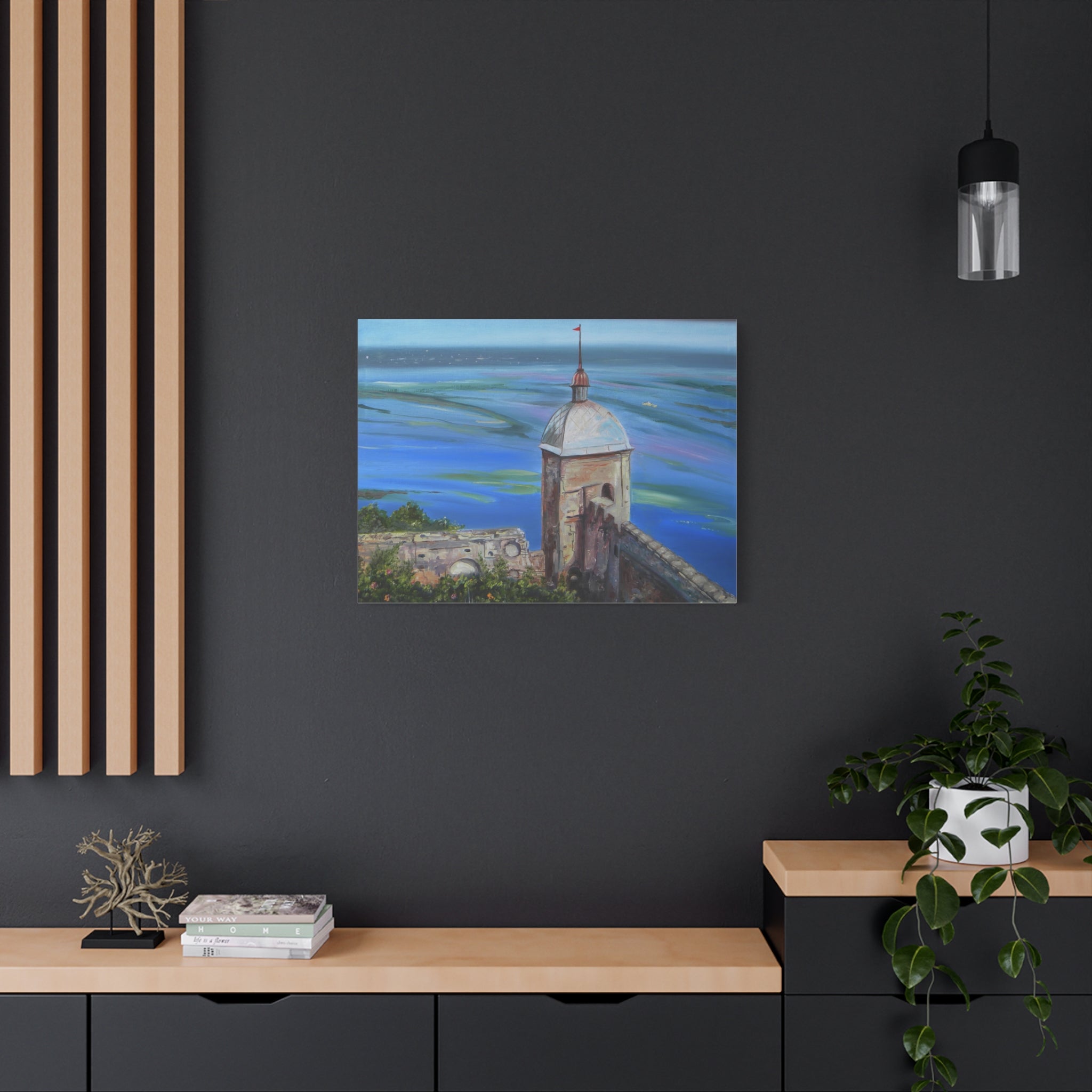 Art print of a coastal scene with a tower on a dark wall above a wooden shelf.