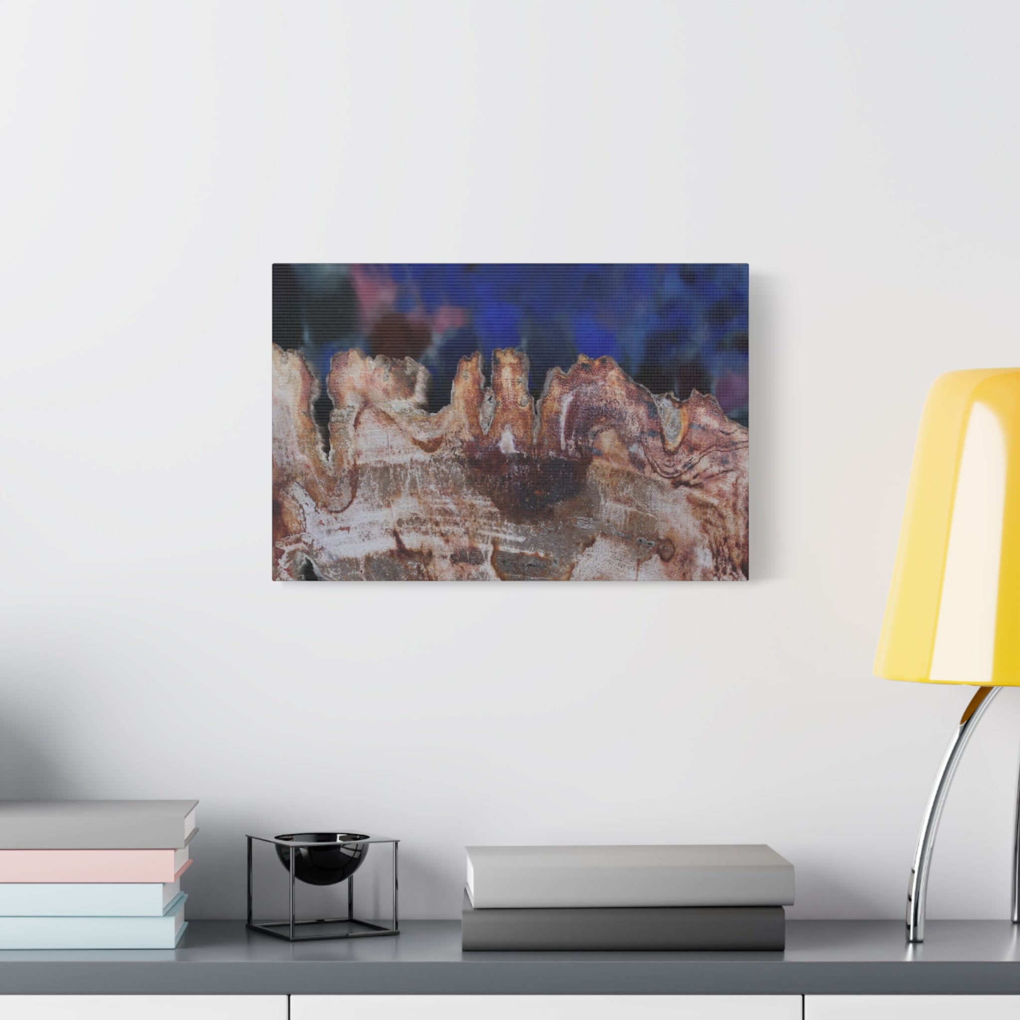 Abstract art piece on a wall above a table with books and a lamp.