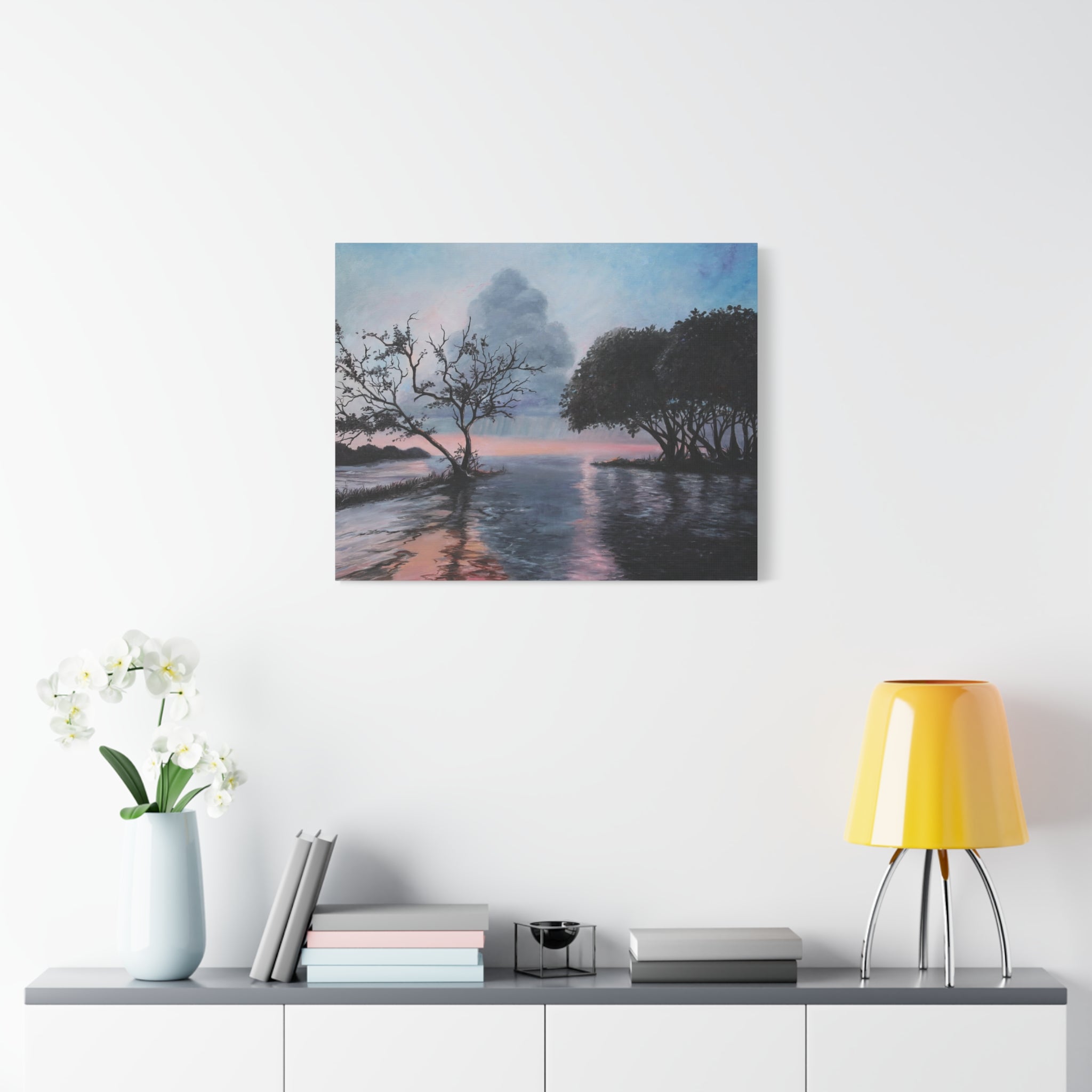 Framed artwork of a landscape with trees and water on a wall above a shelf with decor items.