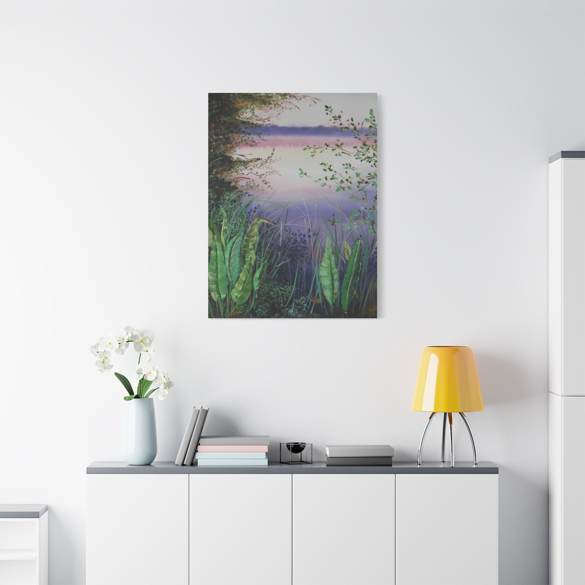 Canvas print of a nature scene hanging on a white wall above a desk with a lamp and books.